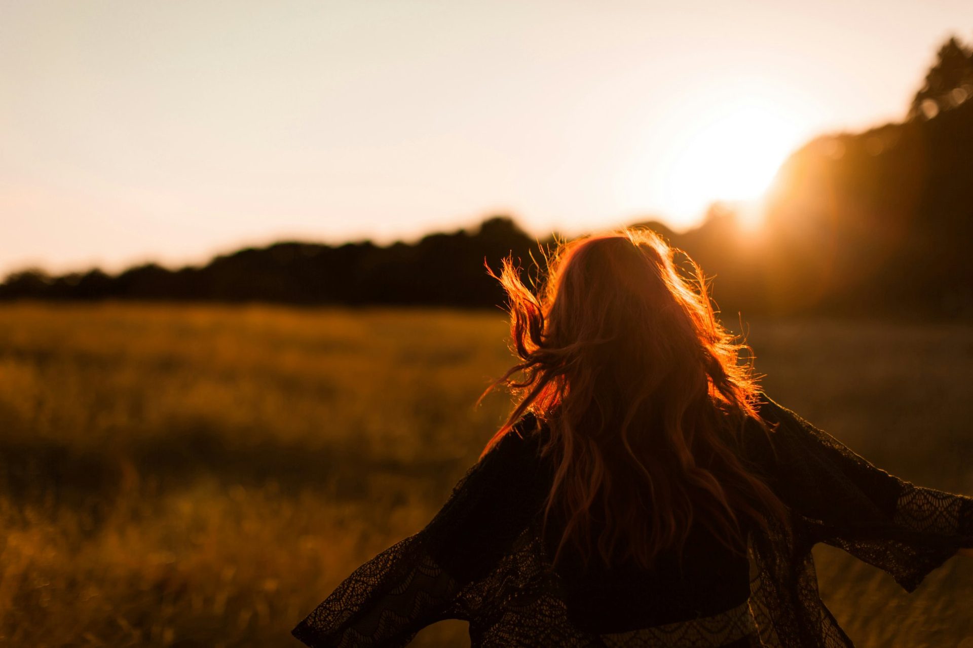 A woman standing in a golden field at sunrise, silhouetted against warm light