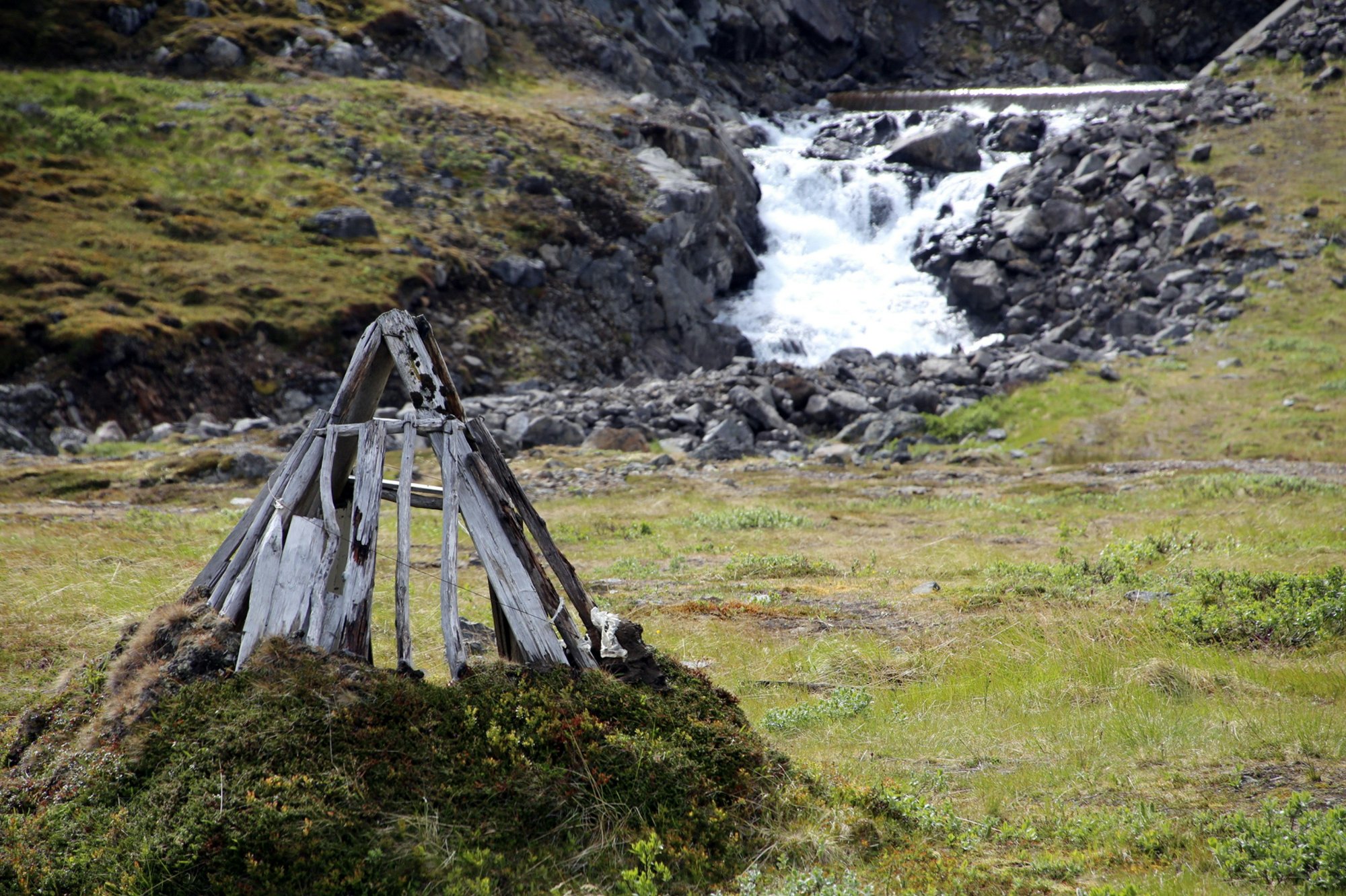 Ancient Sámi wooden shelter in subarctic landscape with waterfall – where dream traditions endure at the edge of the world