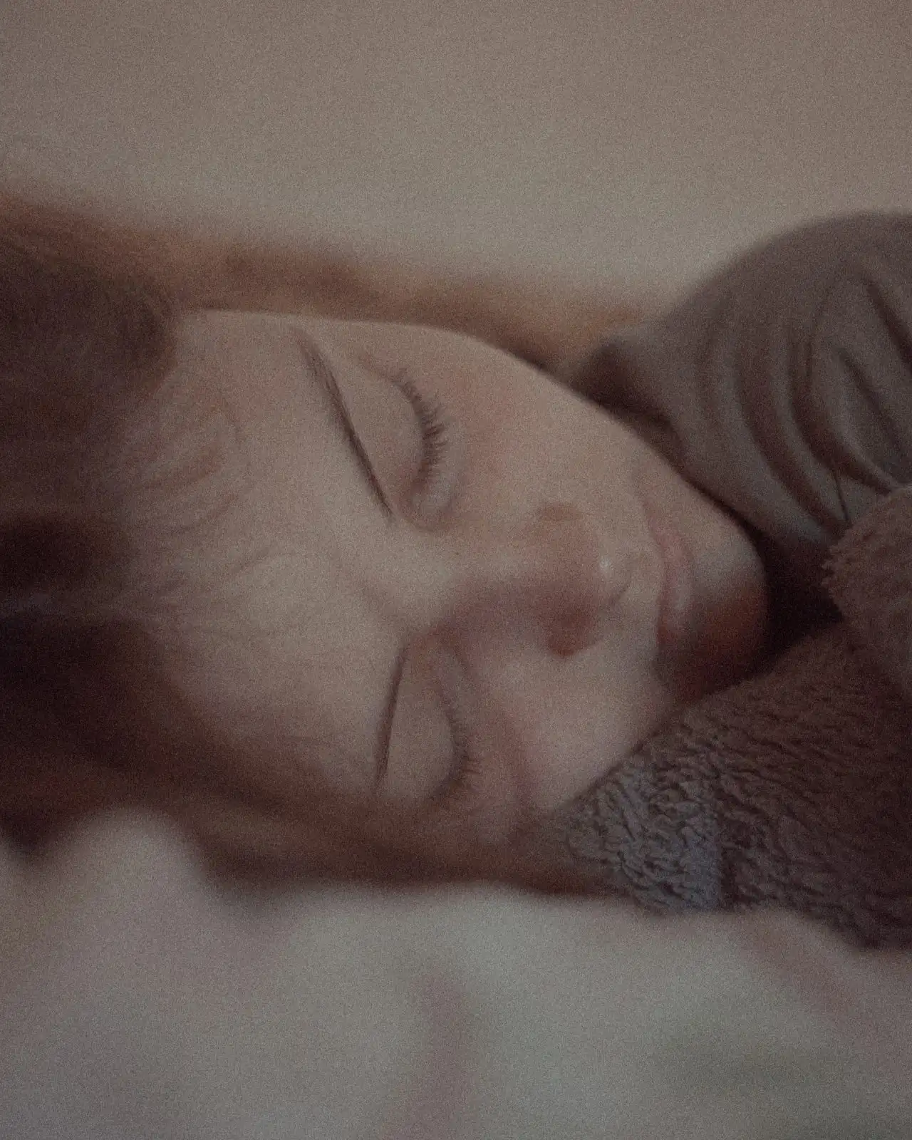 A sleeping face close up on a pillow in warm dim light, eyes closed, the image soft and grainy