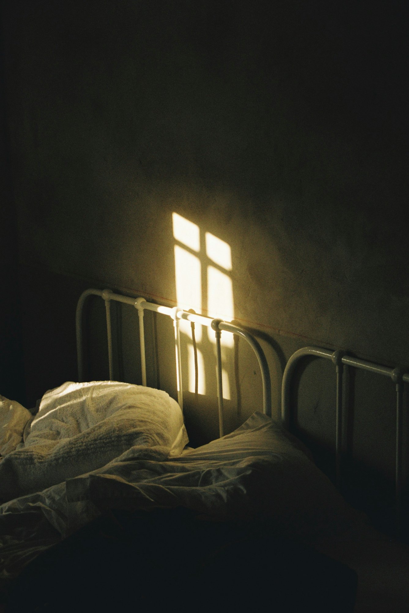 Dark bedroom with light casting through a window onto an empty bed